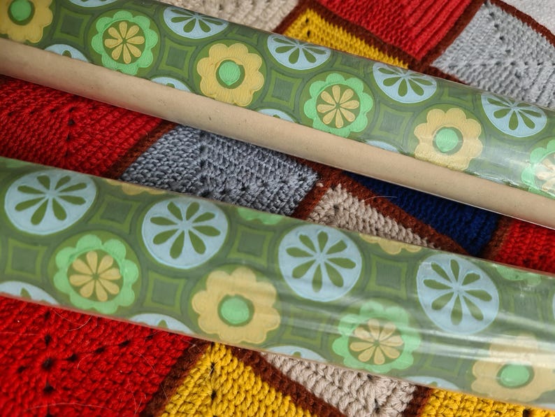 Puede incluir: Dos rollos de papel pintado vintage con un patr&oacute;n floral repetido en tonos verdes, amarillos y azules. El papel pintado est&aacute; enrollado en tubos de cart&oacute;n. El fondo es un colorido patchwork de cuadrados de ganchillo.