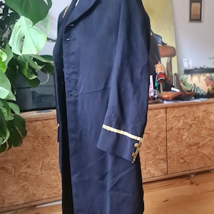 May include: A navy blue military-style coat with gold trim on the collar, cuffs, and epaulets. The coat has a double-breasted design with multiple buttons and a long, tailored fit. The coat is displayed on a mannequin.