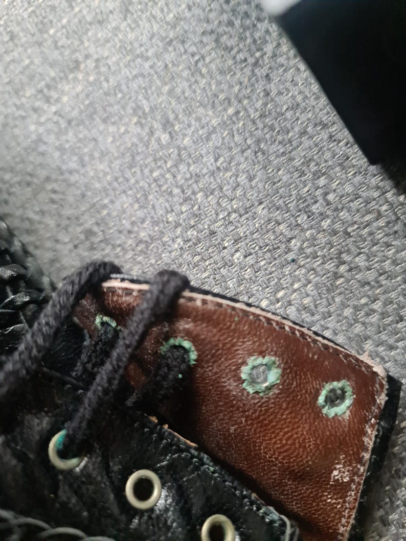 May include: Close-up of a black leather boot with brown leather lining. The boot has a lace-up closure and metal eyelets. The lining has several small, circular holes with a turquoise-colored border.