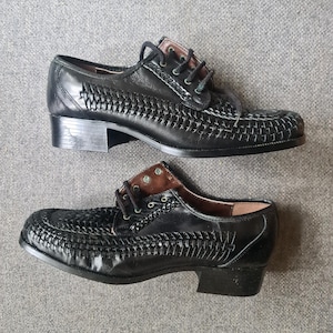 May include: A pair of black leather shoes with a woven design. The shoes have a low heel and a lace-up closure.