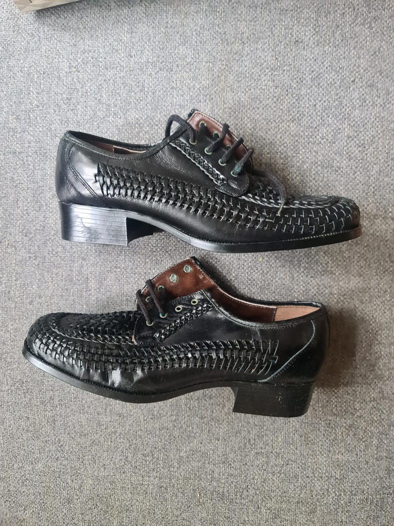 May include: A pair of black leather shoes with a woven design. The shoes have a low heel and a lace-up closure.