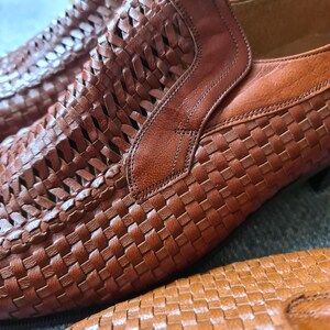 May include: A pair of brown leather shoes with a woven pattern. The shoes have a slip-on design and a pointed toe.