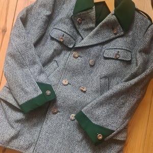 May include: A gray tweed double-breasted coat with dark green collar and cuffs. The coat has four front pockets and decorative wooden buttons. The coat is hanging on a wooden hanger.