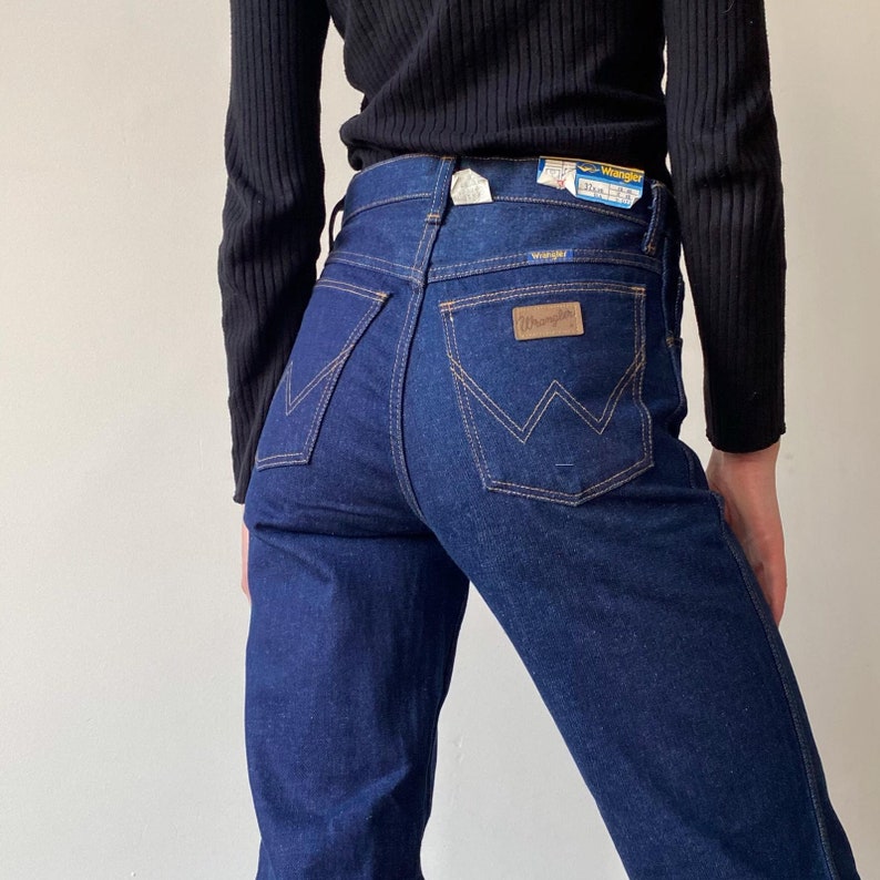 Pode incluir: Um par de cal&ccedil;as de ganga azul escuro com um remendo de couro castanho que diz "Wrangler" no bolso de tr&aacute;s.