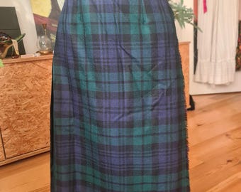 May include: A vintage tartan skirt in green, blue, and black. The skirt has a classic plaid pattern and a straight cut. The fabric looks like a woven material, with a simple waistband and a fringed edge. The skirt is approximately 76 cm in length.