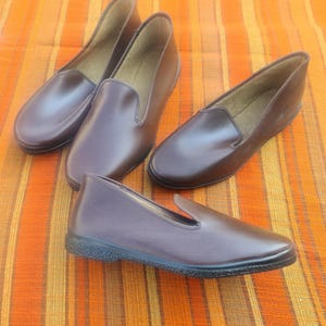 Könnte beinhalten: Drei Paar braune Slipper aus Leder. Die Schuhe haben ein schlichtes Design und sind aus weichem, geschmeidigem Leder gefertigt.