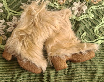 Puede incluir: Un par de botas de piel sintética de color beige claro con tacón grueso. Las botas están hechas de un material suave y esponjoso y tienen una suela de plataforma. Las botas están sobre una superficie verde estampada.