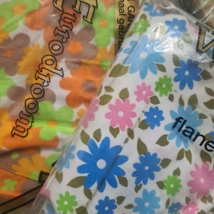 May include: Two packages of fabric with floral patterns. One package has a white background with blue, pink, and green flowers. The other package has a white background with orange, yellow, and green flowers. The text "Eurotoom" is printed on the orange and yellow package. The text "flanel" is printed on the white and blue package.