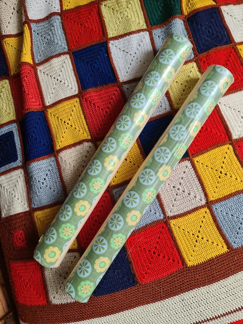 Puede incluir: Dos rollos de papel de regalo verde con un estampado floral de flores azul claro y amarillas. Los rollos est&aacute;n sobre una colorida manta de ganchillo patchwork con cuadrados rojos, amarillos, azules y blancos.