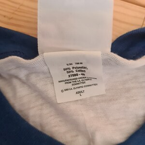 May include: White tag with black text, 5/83 788 M 50% Polyester, 50% Cotton 27590-49 MANUFACTURED UNDER LICENSE FROM THE LA. OLYMPIC COMMITTEE &copy; 1980 LA. OLYMPIC COMMITTEE ADULT L