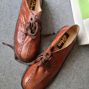 May include: A pair of brown leather lace-up shoes with stitching detail. The shoes have a rounded toe and a thick sole. The brand name "BOGUE" is visible on the inside of the shoes.