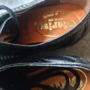 May include: Close-up of the inside of a black leather shoe with a brown leather insole. The insole has the word "Clarks" printed on it in gold lettering.