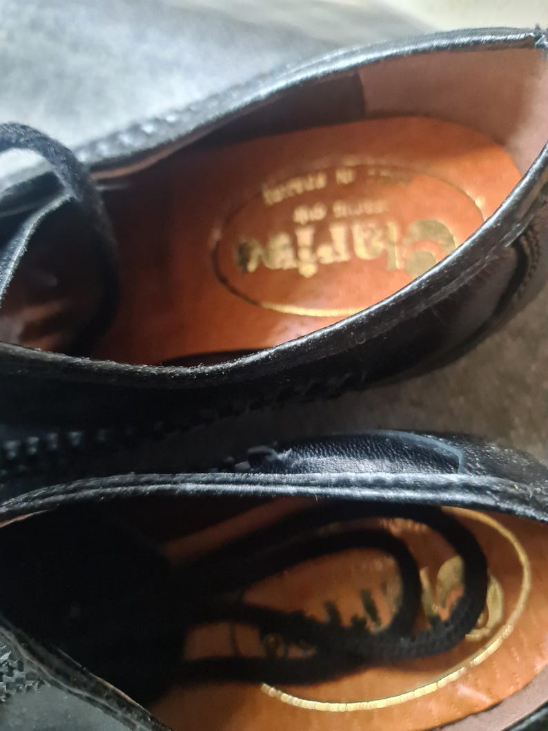 May include: Close-up of the inside of a black leather shoe with a brown leather insole. The insole has the word "Clarks" printed on it in gold lettering.
