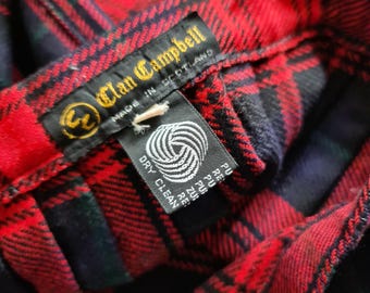 May include: A close-up of a red, black, and green tartan fabric. The label reads "Clan Campbell MADE IN SCOTLAND" and includes a "DRY CLEAN" tag. The fabric displays a classic Scottish plaid design.