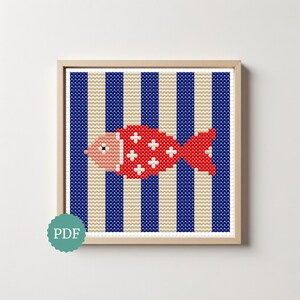 May include: A cross-stitch pattern featuring a red fish with white cross-shaped accents on a background of vertical navy blue and cream stripes, framed in a light wood square frame, with a teal circular PDF icon in the bottom left corner.