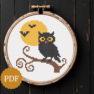 May include: Cross-stitch design featuring a black owl perched on a branch, set against a yellow moon with a bat silhouette. The design is framed in a wooden embroidery hoop. The word "PDF" is printed on a gold sticker.