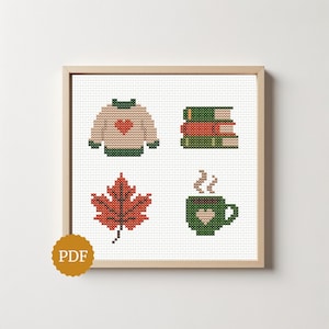 May include: A cross stitch pattern featuring four icons: a beige sweater with a red heart, a stack of three books in green and red, a red maple leaf, and a green mug with a heart and steam, all framed in a light wood square frame.
