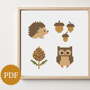May include: Cross-stitch artwork depicting woodland creatures and elements. The framed piece includes a hedgehog, acorns, a pinecone, and an owl, all in brown and tan thread on a white background. The image includes a PDF icon.