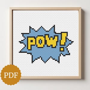 May include: Cross-stitch artwork in a wooden frame. The design features the word "POW!" in yellow letters within a blue burst shape, with black outlines. The background is white. A PDF logo is in the bottom left corner.