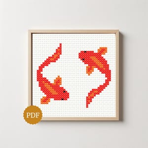 May include: A cross-stitch pattern featuring two koi fish rendered in shades of red and orange on a white grid background. The fish are positioned facing each other within a light wood frame. A circular gold badge with the text PDF is visible.