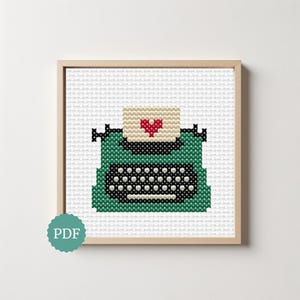 Op de afbeelding: Een kruissteekpatroon met een talingkleurige typemachine met een zwart toetsenbord en een wit vel papier met een klein rood hartje. Het ontwerp is ingelijst in een vierkante lijst van licht hout en een talingkleurig rond icoon met de tekst PDF is zichtbaar.