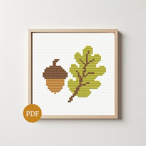 Puede incluir: Un patrón de punto de cruz que muestra una bellota marrón y una hoja de roble verde claro con un tallo marrón oscuro, dentro de un marco de madera clara. Una insignia dorada circular con el texto PDF se sitúa en la esquina inferior izquierda.