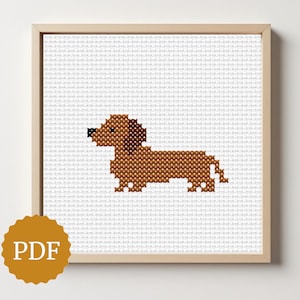 Könnte beinhalten: Gerahmtes Kreuzstichbild eines braunen Dackelhundes. Der Hund befindet sich auf einem weißen Kreuzstichhintergrund in einem hellbraunen Rahmen. Unten links befindet sich ein goldenes PDF-Logo. Thema: Handwerk.