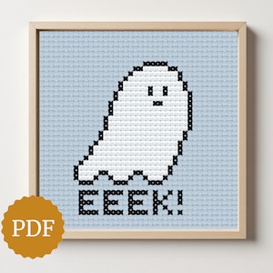 Op de afbeelding: Kruissteekpatroon van een witte geest met zwarte contouren en details, tegen een lichtblauwe achtergrond. Het woord "EEEK!" is eronder in het zwart gestikt. Het kunstwerk is ingelijst in een licht houten frame. Een PDF-pictogram staat linksonder.