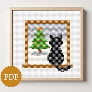 May include: Cross-stitch art of a black cat silhouette looking out a window at a Christmas tree. The tree is green with red and yellow ornaments. The window is framed in brown, and the background shows falling snow. The artwork is in a wooden frame.