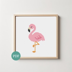 Op de afbeelding: Een kruissteekpatroon met een roze flamingo met een zwart-getipte snavel en oranje poten, weergegeven in een vierkante lijst van licht hout. Een blauwgroene ronde badge met de witte tekst PDF bevindt zich in de linkerbenedenhoek.