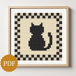 Może przedstawiać: Sztuka haftu krzyżykowego przedstawiająca sylwetkę czarnego kota na kremowym tle, oprawiona w drewnianą ramę. Kot jest wyśrodkowany w kwadracie, otoczony czarno-kremowym wzorem szachownicy. Widoczna ikona PDF.