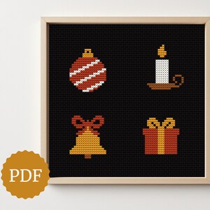 May include: Cross-stitch art print featuring four Christmas-themed icons: a red and white striped ornament, a candle, a gold bell with a red bow, and a wrapped gift. The artwork is framed in a light wood frame.