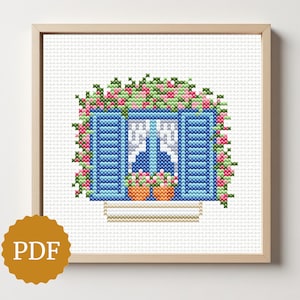 May include: Cross-stitch pattern of a blue window with shutters, adorned with pink and green flowers. Two orange flower pots sit below the window. The artwork is framed in a light wood frame. A PDF icon is in the lower left corner.