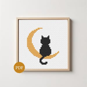 Peut inclure: Un motif de point de croix encadré représentant un chat noir assis sur un croissant de lune doré. Le motif est posé sur un fond blanc et est encadré dans un cadre en bois brun clair. Une icône PDF est dans le coin inférieur gauche.