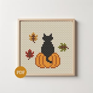 May include: A cross-stitch pattern in a light wood frame featuring a black cat sitting on an orange pumpkin, surrounded by three autumn leaves in yellow, red, and green. A circular gold badge with the text PDF is visible in the bottom left corner.