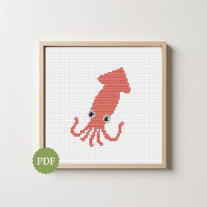 May include: A framed cross-stitch of a coral-colored squid with black and white eyes and curled tentacles. The artwork is set against a white background and framed in a light wood. A green PDF logo is in the lower left corner.