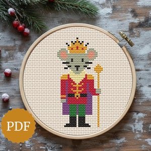 Può includere: Ricamo a punto croce di un re topo con una corona d'oro e uno scettro. Il topo indossa una giacca rossa, un mantello viola e pantaloni verdi. Il ricamo è in un telaio di legno, con un logo PDF.