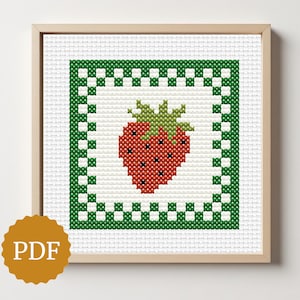 May include: A framed cross-stitch of a strawberry. The red strawberry with green leaves is set against a white background, framed by a green border. The artwork is in a wooden frame, with a PDF icon in the lower left corner.