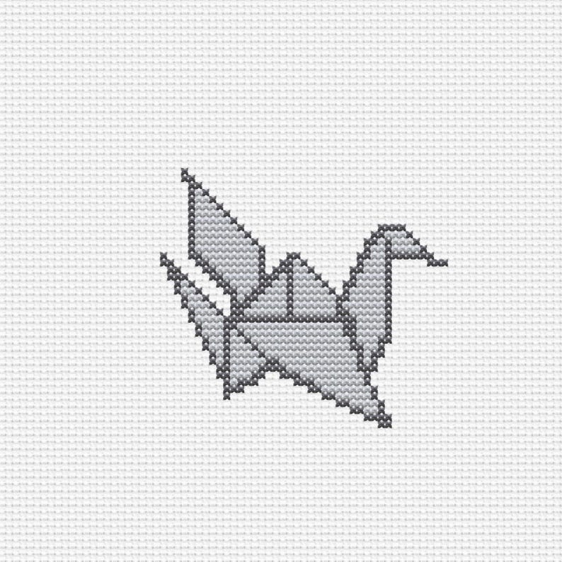 Op de afbeelding: Een kruissteekpatroon met een gestileerde origami-kraanvogel in grijstinten. Het ontwerp bestaat uit individuele X-vormige steken op een witte rasterstof, wat een geometrische vogelvorm cre&euml;ert met puntige vleugels en een staart.