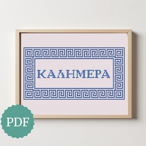 May include: A framed cross-stitch design with the Greek word "ΚΑΛΗΜΕΡΑ" in blue, surrounded by a blue Greek key border on a pink background. The frame is light brown. A green PDF icon is in the lower left corner.