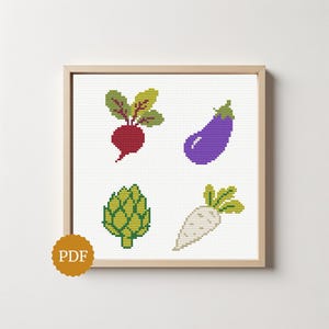 May include: A cross-stitch pattern featuring four vegetables: a red beetroot with green leaves, a purple aubergine, a green artichoke, and a white daikon radish. The design is displayed in a light wood frame with a gold circular PDF icon in the corner.