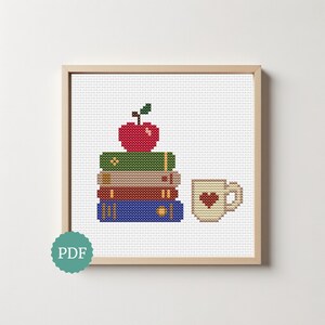 Pode incluir: Um padrão de ponto cruz numa moldura de madeira clara com uma pilha de quatro livros em verde, bege, vermelho e azul com uma maçã vermelha no topo e uma caneca bege com um coração vermelho à direita. Um ícone PDF circular turquesa está abaixo.