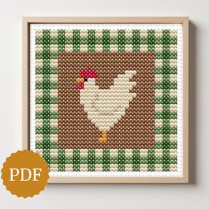 May include: Framed cross-stitch artwork featuring a white chicken with a red comb and yellow feet, set against a brown background. The design is framed by a green and white checkered pattern. The artwork is in a wooden frame.