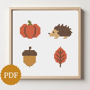 Può includere: Un motivo a punto croce incorniciato con disegni a tema autunnale. L'opera d'arte comprende una zucca, un riccio, una ghianda e una foglia, il tutto in calde tonalità terrose. L'immagine ha un logo PDF nell'angolo in basso a sinistra.