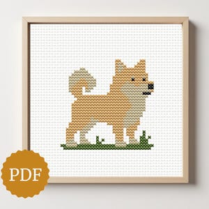 May include: A framed cross-stitch of a Shiba Inu dog in shades of tan and white, standing on green grass. The artwork is in a light wooden frame and features a PDF logo in the lower left corner.