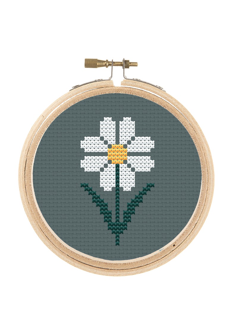 May include: A white daisy with a yellow center is embroidered on a teal fabric in a wooden embroidery hoop.
