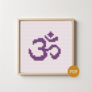 Puede incluir: Un patrón de punto de cruz que presenta un símbolo Om de color púrpura centrado sobre una tela de rejilla blanca. El diseño se muestra dentro de un marco cuadrado de madera clara. Una pequeña insignia circular dorada con las letras PDF está en la esquina.