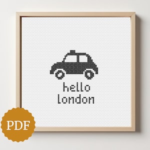 Puede incluir: Un cuadro bordado a punto de cruz con un taxi negro de Londres y la frase "hello london" en una fuente sencilla y moderna. La obra de arte está sobre un fondo blanco y enmarcada en madera clara.