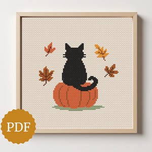 May include: A framed cross-stitch design featuring a black cat sitting on an orange pumpkin, surrounded by autumn leaves. The artwork is set against a beige background, with a PDF logo in the lower left corner.