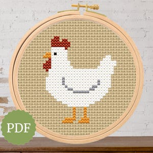 May include: A cross-stitch design of a white chicken with red comb and yellow beak and feet, set in a wooden embroidery hoop. The background is tan fabric. A green circle with the text "PDF" is in the lower left.